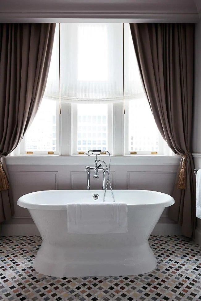 elegant bathtub on multi-color marble floor with window drapery