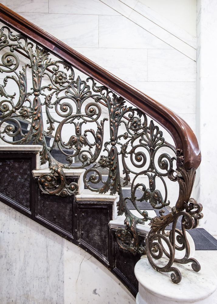 Ornate wrought-iron staircase railing with scrolling floral motifs and marble stairs inside the historic Chicago Athletic Association building.